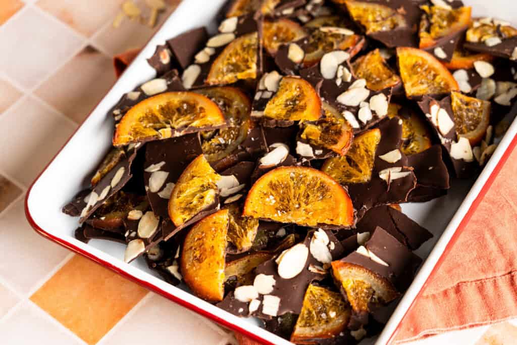 A tray of dark chocolate bark with candied orange slices, sliced almonds and flaky sea salt