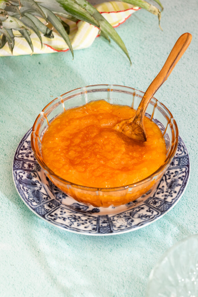 Close-up of pineapple and passion fruit jam in a glass bowl with a wooden spoon.