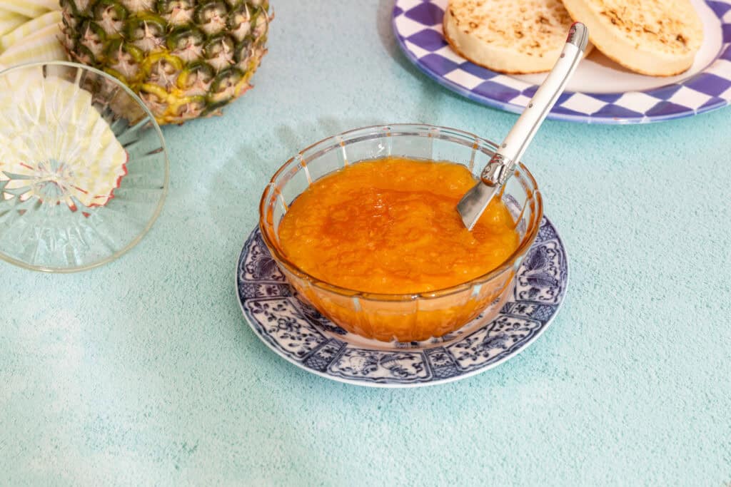 Close-up of pineapple and passion fruit jam in a glass bowl with a wooden spoon.